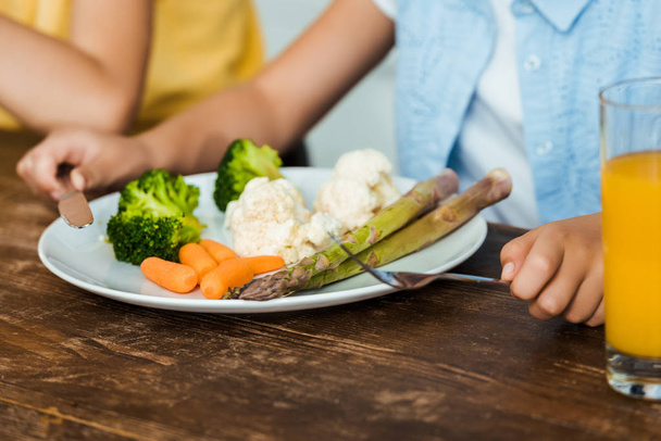close-up partial view of child holding fork and knife while eating healthy vegetables - Foto, Imagem