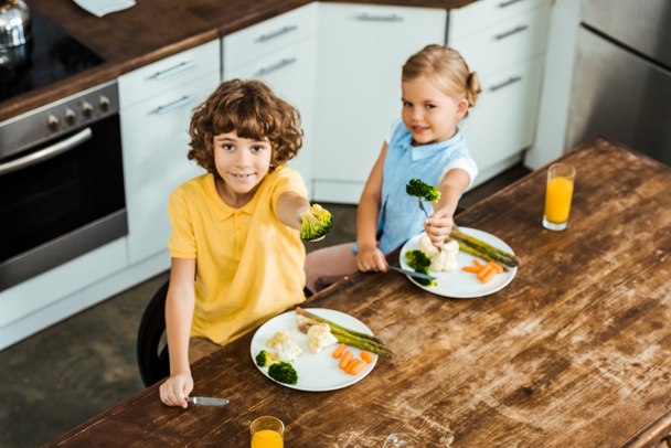 high angle view of kids holding forks with broccoli and smiling at camera - Фото, зображення