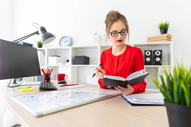 Een jong meisje zit aan een tafel in het kantoor en een zwarte marker in haar hand houdt. Het meisje werkt met een computer, Kladblok en een magneetbord. - Foto, afbeelding
