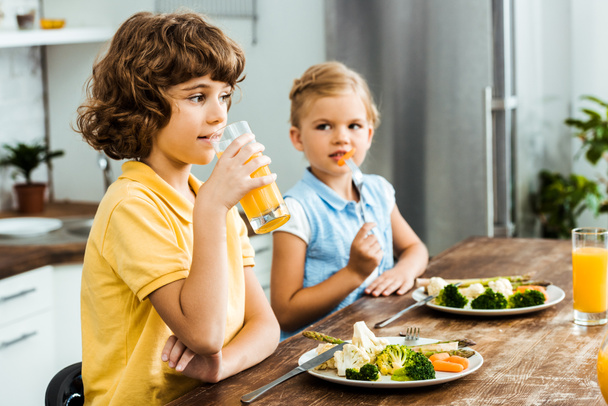 adorable kids sitting together at table, eating vegetables and drinking juice - Фото, изображение