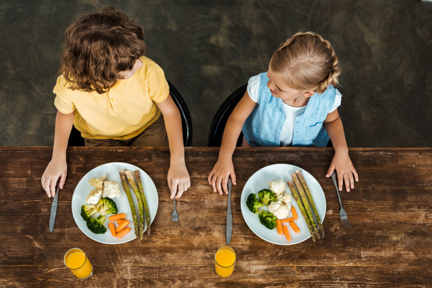 magas szög kilátás imádnivaló gyerekek eszik egészséges zöldség és néztek egymásra - Fotó, kép