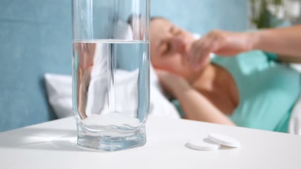 ベッドで横になっていると、頭痛に苦しむ若い女性の隣にベッドサイド テーブルの上に立って水のガラスのスローモーション映像 - 映像、動画