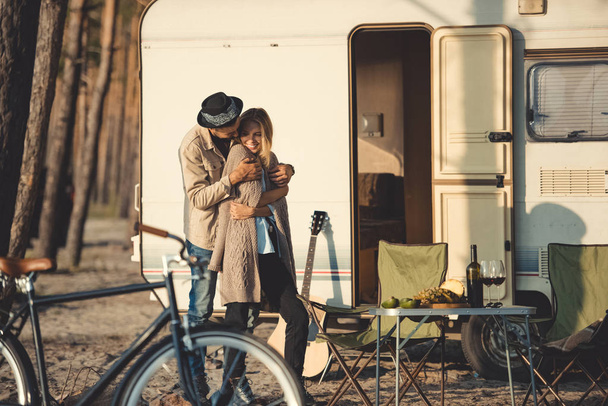 νεαρός άνδρας αγκαλιάζει ευτυχισμένη γυναίκα κοντά campervan με ποδήλατο - Φωτογραφία, εικόνα