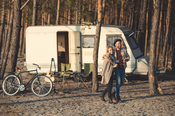 man hugging girlfriend with wine and walking near campervan - Photo, Image