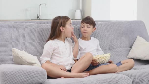Cute child eat popcorn on sofa and watch tv - Záběry, video