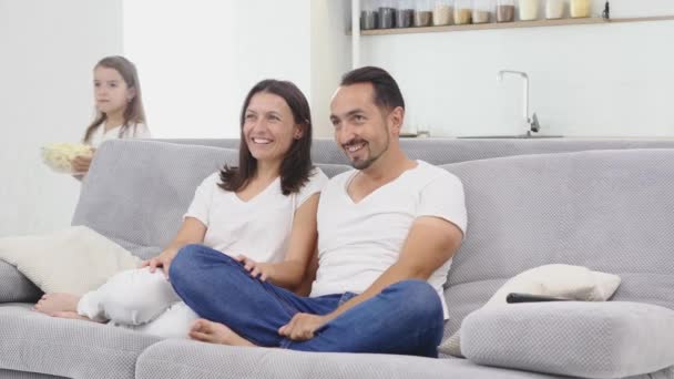 Young couple watching tv with popcorn in the living room. children brings popcorn on the couch - Πλάνα, βίντεο