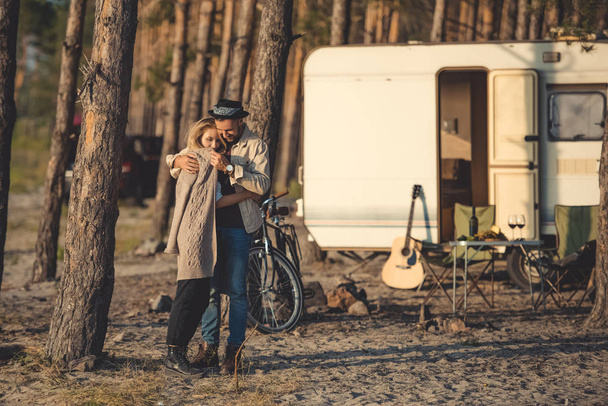 beautiful happy couple embracing in camp with trailer, bicycle and guitar - Photo, Image