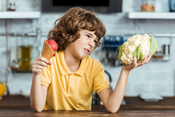 unhappy child holding delicious sweet ice cream and healthy cauliflower  - Foto, imagen
