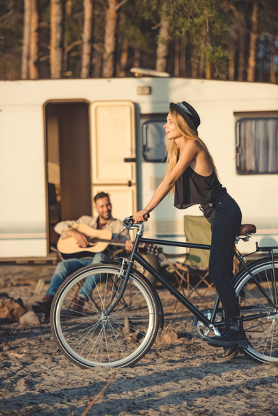 enfoque selectivo de la hermosa mujer con la bicicleta y el hombre tocando la guitarra cerca de autocaravana
 - Foto, imagen