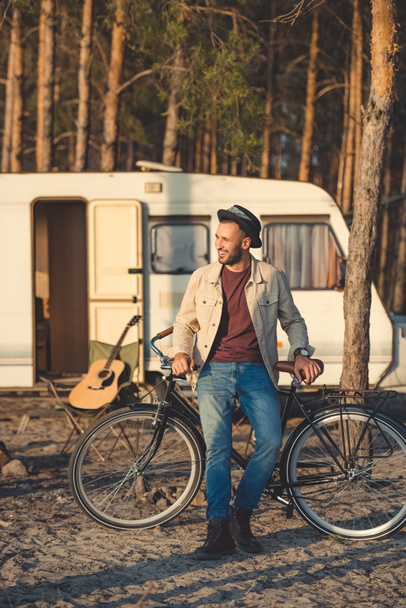 young handsome man leaning on bicycle near campervan in forest - Photo, Image