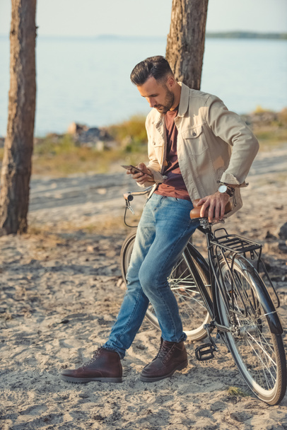 young man using smartphone and leaning on bicycle - Photo, image