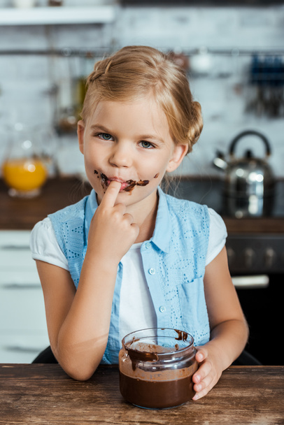 αξιολάτρευτο παιδί τρώει άλειμμα σοκολάτας και να χαμογελά στη φωτογραφική μηχανή  - Φωτογραφία, εικόνα