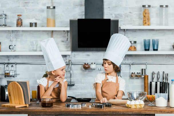 adorable little children in chef hats and aprons cooking together in kitchen  - Photo, Image
