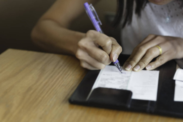 Το χέρι της γυναίκας υπογραφή με πένα σε χαρτί γλιστρά δαπάνη πληρωμής με πιστωτική κάρτα. - Φωτογραφία, εικόνα