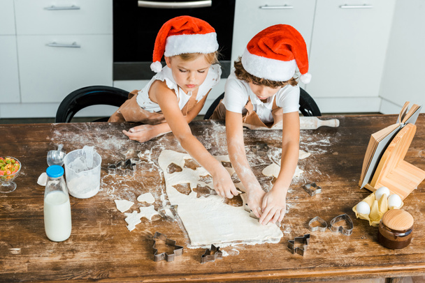high angle view of adorable chldren in santa hats and aprons preparing christmas cookies together - Photo, Image