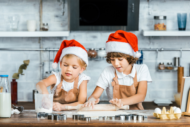 αξιολάτρευτο παιδιών Καπέλα santa και ποδιές προετοιμασία χριστουγεννιάτικα μπισκότα μαζί - Φωτογραφία, εικόνα