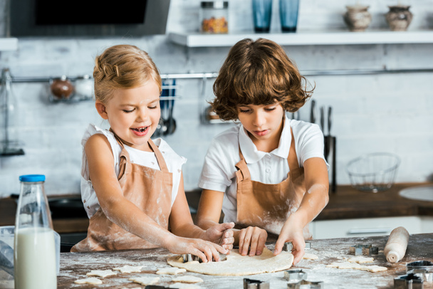 adorable smiling children in aprons preparing dough for tasty cookies - Fotografie, Obrázek