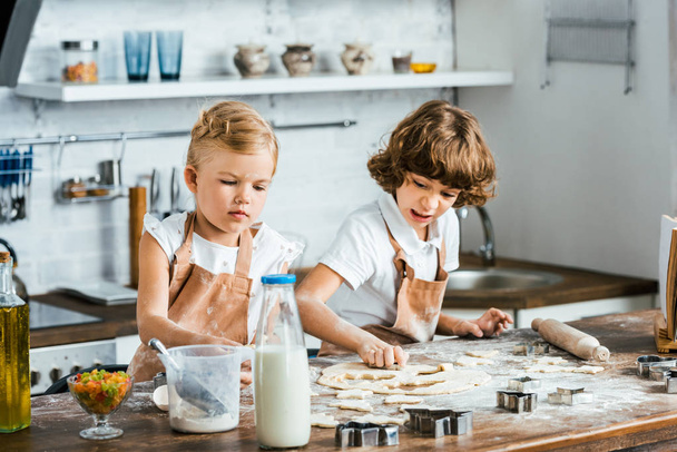 adorables niños en delantales preparando masa para sabrosas galletas
 - Foto, Imagen