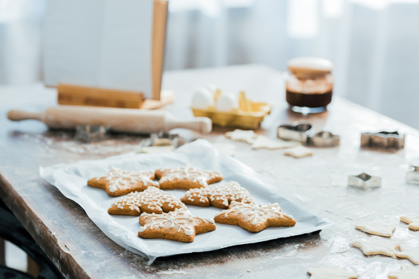 vergrote weergave van heerlijke gember koekjes op bakken lade, kookboek en ingrediënten op tafel - Foto, afbeelding