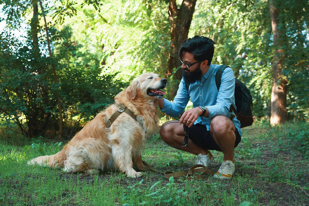 Un joven guapo con recuperador de oro al aire libre. Hombre en una hierba verde con perro. Cynologist. Mejores amigos
 - Foto, imagen