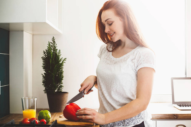 Une jeune femme dans la cuisine prépare une salade. Elle coupe le rouge
 - Photo, image