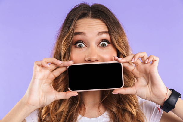 Image of emotional woman isolated over purple wall background showing display of mobile phone. - Foto, Imagen