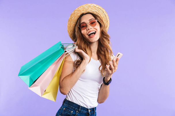 Photo of amazing happy cute woman isolated over purple wall background holding shopping bags using mobile phone. - Фото, изображение