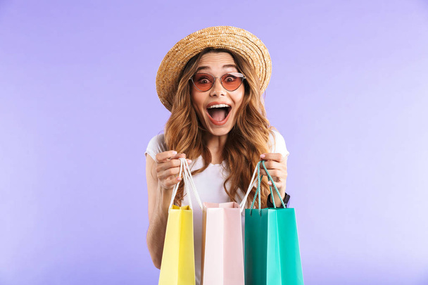 Photo of excited surprised cute woman isolated over purple wall background holding shopping bags. - Fotografie, Obrázek