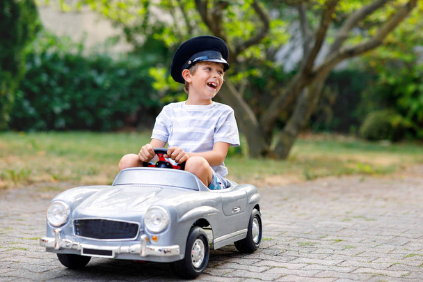 Garçon heureux jouant avec une grande vieille voiture jouet dans le jardin d'été, à l'extérieur. Enfant sain conduisant un vieux taxi de voiture vintage. Enfant riant et souriant. Famille, enfance, mode de vie concept
 - Photo, image