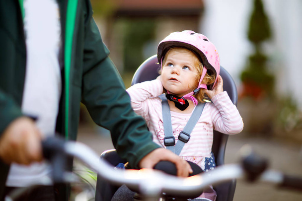 Portré egy kislányról, bukósisakkal a fején, aki bicikliülésben ül, és az apja vagy az anyja biciklivel. Biztonságos és gyermekvédelmi koncepció. Családi és hétvégi kirándulások. - Fotó, kép