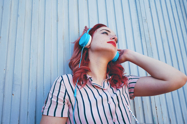 εξωτερική πορτρέτο του όμορφη νεαρή γυναίκα με τα κόκκινα μαλλιά, φοράει ακουστικά μπλε  - Φωτογραφία, εικόνα