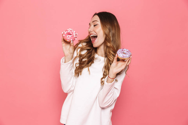 Portrait of a happy young woman showing donuts isolated over pink background - Фото, изображение