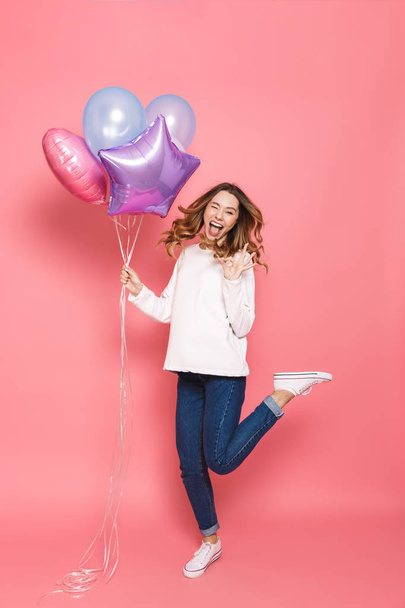 Full length portrait of a cheerful young woman holding bunch of air balloons while jumping isolated over pink background, showing ok - Φωτογραφία, εικόνα