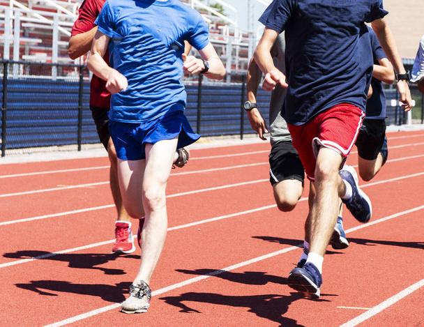 High school boys training together in the bright sunshine of summer on a red track in fron of the bleachers. - Photo, Image