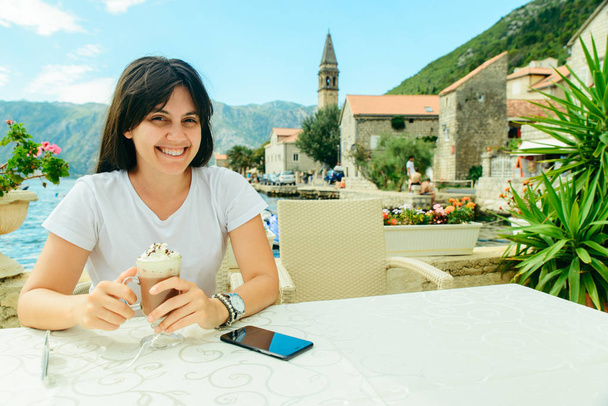 woman sitting in cafe on perast seaside in montenegro eating ice cream. summer vacation - Photo, Image