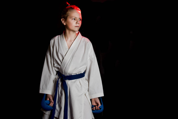 Young boy training karate on black background. Blue belt and mitts, karate gloves. Cute teenage emotions boy on training. Shock hand and scream. - Photo, Image
