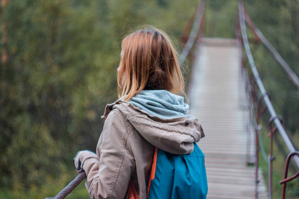 Girl traveler with red long hair on forest suspension bridge  - Foto, Imagen