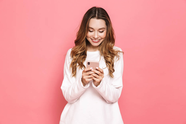 Portrait of a happy young woman using mobile phone isolated over pink background - Fotografie, Obrázek