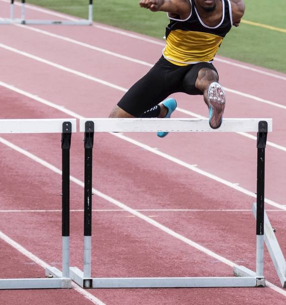 An African American high school track and field athlete racing over a hurdle. - Photo, Image