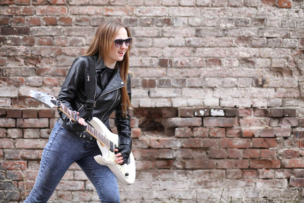  Ένα κορίτσι μουσικός βράχου σε ένα δερμάτινο σακάκι με μια κιθάρα  - Φωτογραφία, εικόνα