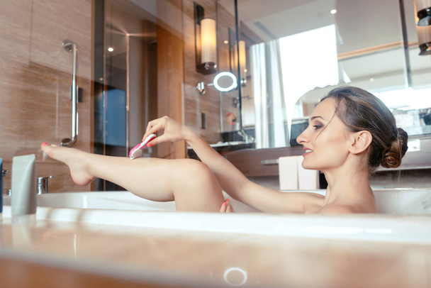 Mulher tomando banho na banheira do hotel agarrando seu barbeador
 - Foto, Imagem
