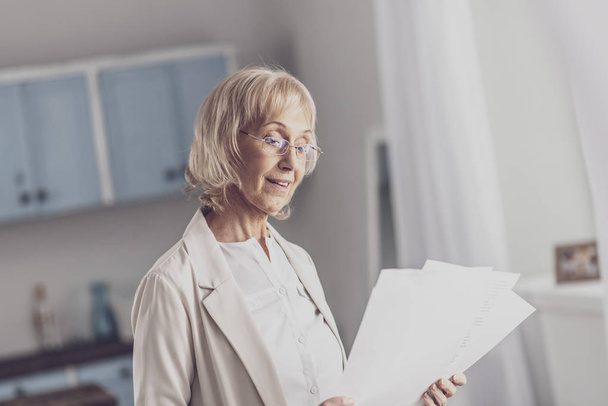 Elderly woman reading reports standing in the kitchen - Fotoğraf, Görsel