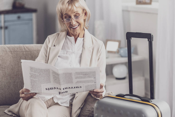 Woman reading weekly newspaper before going to airport - Photo, Image