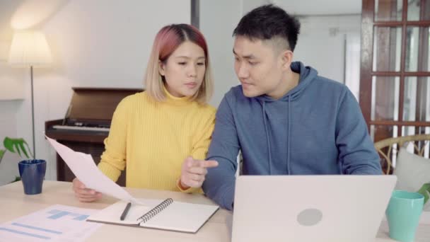 Young asian couple managing finances, reviewing their bank accounts using laptop computer and calculator at modern home. Woman and man doing paperwork together, paying taxes online on notebook pc. - Metraje, vídeo
