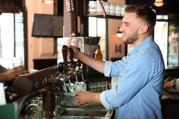 Bartender working at beer tap in pub - Фото, изображение