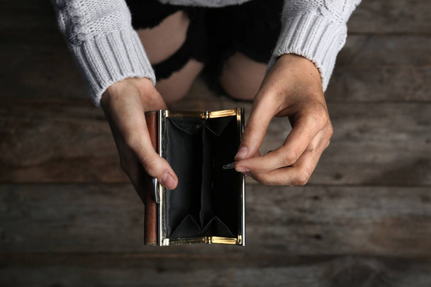 Poor woman holding empty wallet and coin on wooden background, closeup - 写真・画像