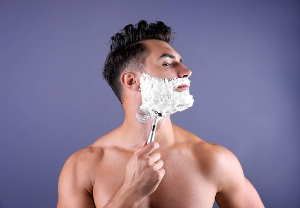 Handsome young man shaving on color background - 写真・画像