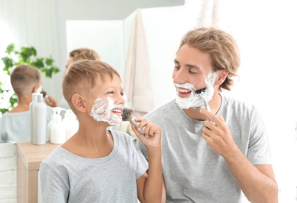 Father and son shaving together on color background - Foto, immagini