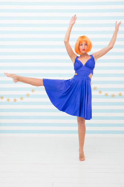 Fun and entertainment. Girl bob wig posing striped background of studio. Create your own mood. Lady red or ginger wig posing in blue dress. Comic and humorous concept. Woman playful mood having fun - Foto, afbeelding
