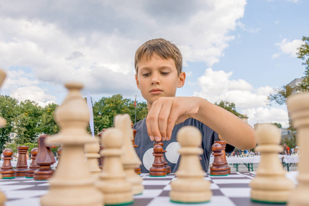 Парень играет в шахматы на улице. Мальчик тщательно обдумывает комбинации шахмат
 - Фото, изображение
